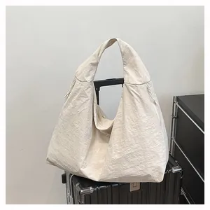Dettaglio della borsa tote in nylon crema con trama increspata posta su una valigia