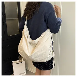 Detail of a large beige nylon crossbody bag with side drawstring and wide strap