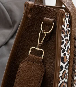 Detail des goldenen Karabinerverschlusses an brauner Ledertasche mit Leopardenmuster