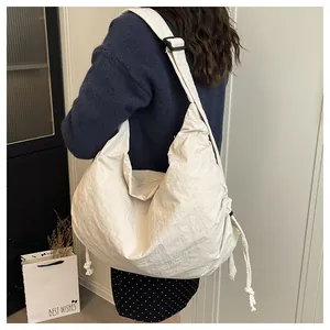 Detail of cream crescent nylon bag featuring side drawstrings and adjustable shoulder strap