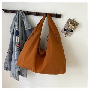Dettaglio borsa tote in nylon caramello con coulisse appesa a un supporto in legno