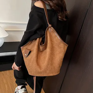 Détail d'un grand sac cabas en daim marron avec anses en cuir porté à l'épaule