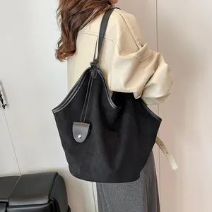Détail d'un grand sac cabas en daim noir avec bandoulière en cuir et pendentif décoratif