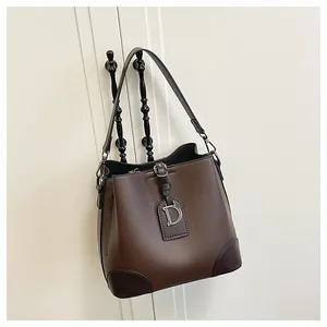 Dettaglio borsa a secchiello marrone scuro con texture in pelle e logo metallico D frontale