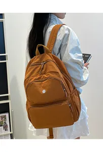 Vista laterale dello zaino in nylon caramello con tasche a zip e dettaglio logo metallico