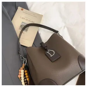 Dettaglio borsa a secchiello in pelle marrone con ciondolo D argento e decoro perline