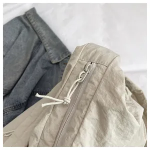 Close-up of cream nylon shoulder bag featuring knotted rope zipper pull and texture