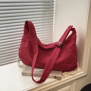 Large burgundy nylon hobo bag with adjustable strap and side drawstrings on a shelf