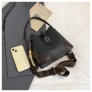 Dettaglio borsa a secchiello vintage in pelle nera con tracolla e ciondolo a D