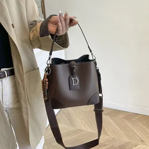 Borsa a secchiello retrò in pelle cioccolato con fibbia a D e ciondolo di perle portata a mano