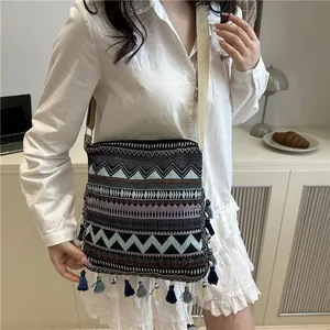 Bohemian geometric woven crossbody bag with colorful fringes for women on table background