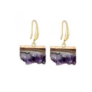 Détail de boucles d'oreilles en améthyste naturelle avec bords bruts et crochets dorés