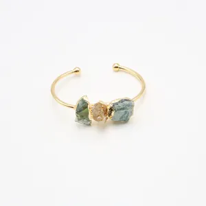 Detalle de brazalete abierto dorado con tres piedras naturales en un engaste hecho a mano