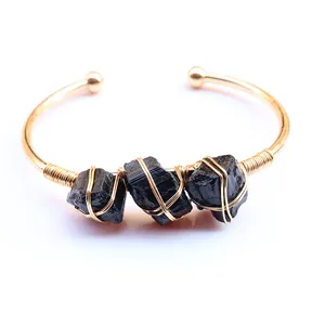 Detail van met koperdraad omwikkelde zwarte ruwe kristalstenen op gouden open armband