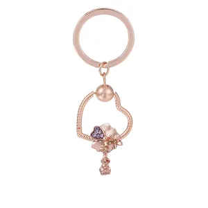 Porte-clés cœur en or rose avec pendentifs fleurs et zircons violets sur fond blanc