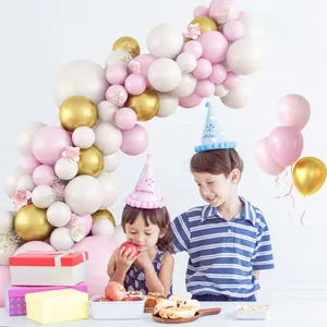 Macaron pink and gold party balloon arch kit with decorative birthday hats on white background