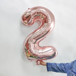 Hand hält einen 32-Zoll rosagoldenen Zahlenballon Nummer 2 für Geburtstagsdekorationen