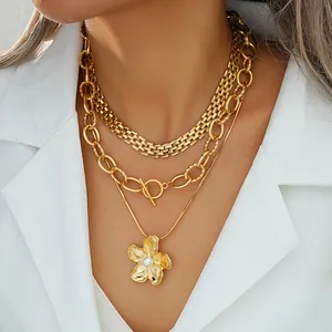 Detalle de collares dorados en capas con colgante de flor y perla y cierre OT en modelo