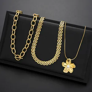 Detalle de colgante de flor dorada con perla y collares de cadena gruesa con cierre OT