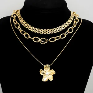 Detalle de collar dorado de tres capas con colgante de flor y cierre de barra en T