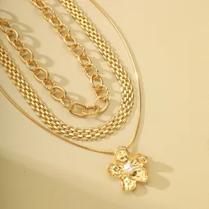 Detalle de collares dorados en capas con eslabones y colgante de flor con perla