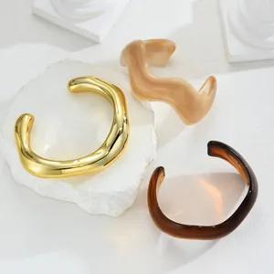 Set of three wavy irregular resin and gold metal open bangles on a stone base