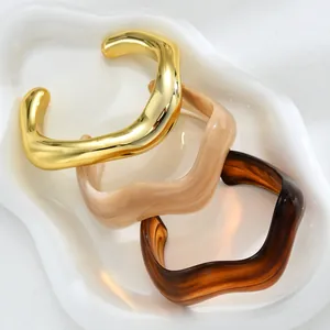 Detailed view of three irregular wave resin and gold metal bangles on a ceramic plate