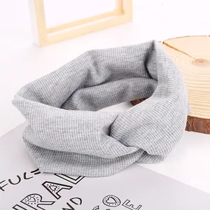 Detail of light grey ribbed knit headband featuring a twist knot cross design on wood base