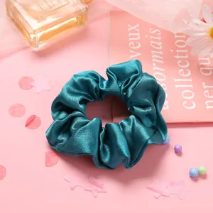 Détail du chouchou en satin vert foncé avec éclat soyeux sur fond rose élégant