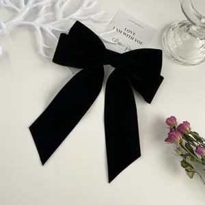 Detail view of a large black velvet bow hair clip with elegant long ribbons on white surface