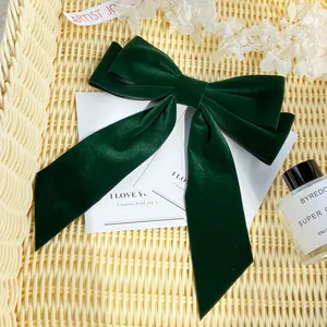 Detailed view of a dark green velvet bow hair clip on a textured beige display tray