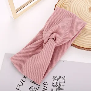 Close-up of ribbed knit dusty pink headband with twist knot design on wooden stand