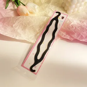 Detail of wavy black plastic hair styling tool in pink dotted packaging on a desk