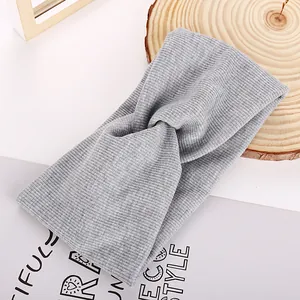 Detail of light grey ribbed knit headband featuring a chic cross knot design on wood