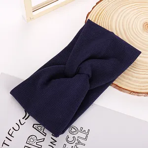 Macro detail of navy blue ribbed knit headband with cross-knot design on white background