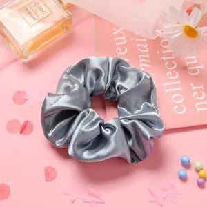 Détail d'un chouchou en satin gris argenté brillant sur un fond décoratif rose