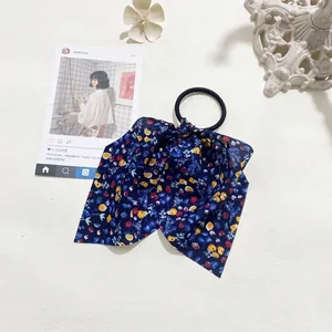 Blue floral bow scrunchie with colorful flower patterns on a white textured desk