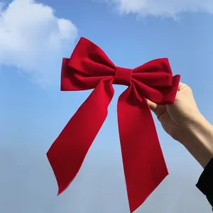 Large red velvet bow hair clip with long ribbons held against a bright blue sky background