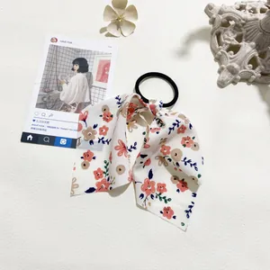 Close-up of chiffon floral bow scrunchie with pink blossoms and green leaves on cream fabric