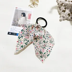 Detail view of floral print ribbon hair scrunchie with pink chiffon bow and green leaf motifs