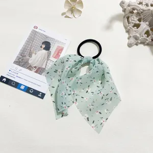 Detail view of light green floral chiffon bow hair scrunchie on a decorative background