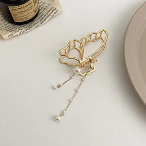 Détail d'une pince à cheveux papillon dorée avec des glands en perles sur fond minimaliste