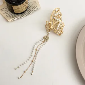 Détail de la pince à cheveux papillon dorée avec perles et longues chaînes à pompons