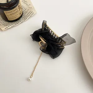 Détail de pince à cheveux dorée avec nœud en maille noire et pompon en perle