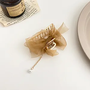 Détail de pince à cheveux dorée avec nœud en organza marron et chaîne à pampille en perle