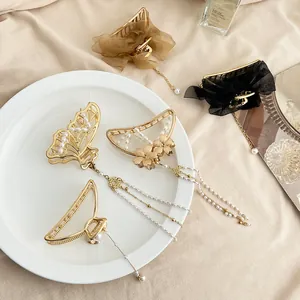 Pinces à cheveux papillon dorées avec perles et longs glands sur assiette blanche