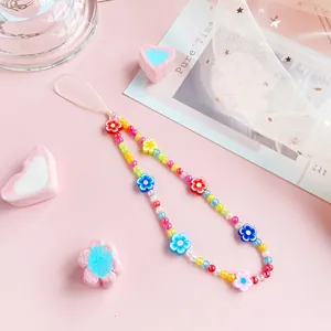 Colorful floral beaded phone strap with resin charms and white cord on pink background