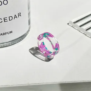 Dettaglio macro dell'anello in resina trasparente con bacche viola e foglie verdi