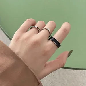Close-up of stacked rings including silver chain, twist designs and black enamel band