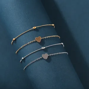 Minimalist gold and silver layered anklet set with heart charms on a blue display stand
